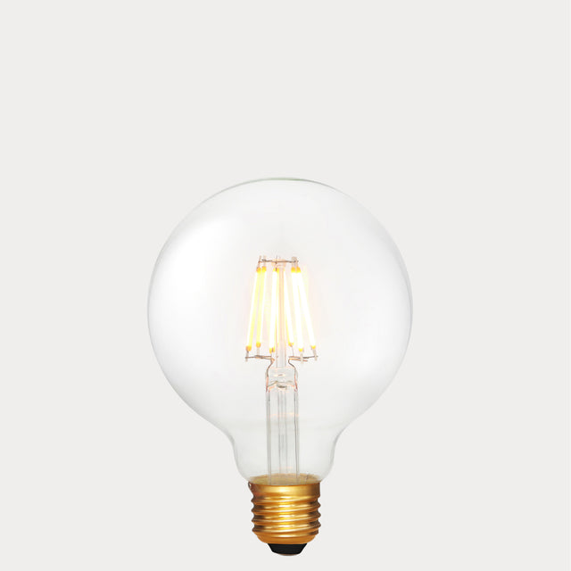 Dulora 6W E27 LED globe bulb in clear glass with 24V compatibility, glowing with 2200K extra warm white light.