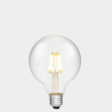 Dulora 8W E27 LED globe bulb in clear glass with AC/DC compatibility, glowing with 2700K warm white light.