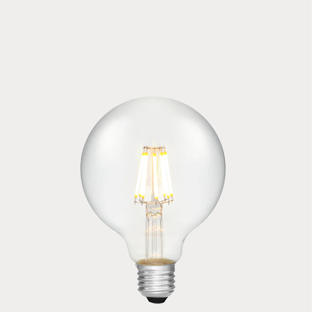 Dulora 8W E27 LED globe bulb in clear glass with AC/DC compatibility, glowing with 2700K warm white light.