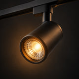 A modern black track spotlight GU10 lamp with a warm glowing light, mounted on a black ceiling track against a dark background.
